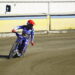 Motocross Rider in Blue Gear and Red Helmet Leaning into a Turn on a Dirt Track Beside Yellow Barriers Behind a Building Edge 15 Czerwca 2020 