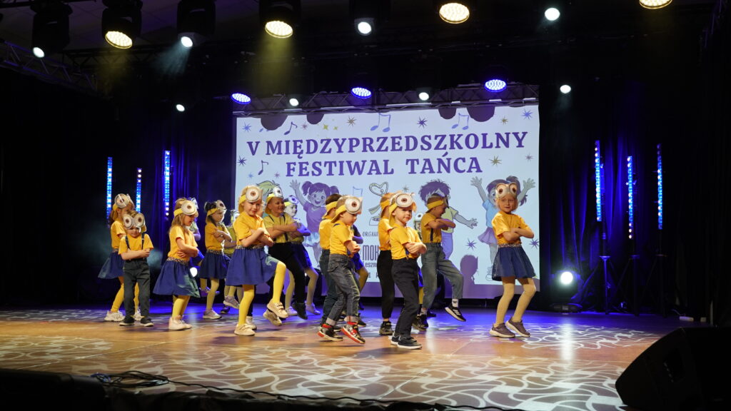 Kids Performing a Dance on Stage in Yellow Shirts and Blue Bottoms with a Banner Reading v MiĘdzyprzedszkolny Festiwal TaŃca in the Background 9 Września 2025  ml 2358