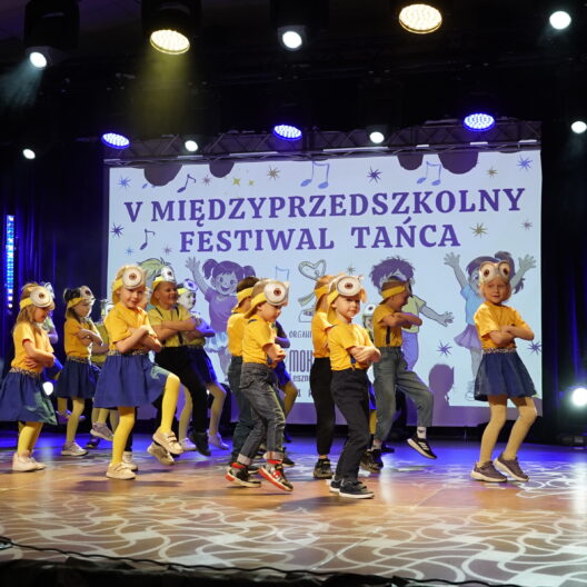 Kids Performing a Dance on Stage in Yellow Shirts and Blue Bottoms with a Banner Reading v MiĘdzyprzedszkolny Festiwal TaŃca in the Background 9 Września 2025  ml 2358