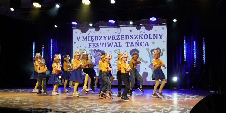 Kids Performing a Dance on Stage in Yellow Shirts and Blue Bottoms with a Banner Reading v MiĘdzyprzedszkolny Festiwal TaŃca in the Background 21 Kwietnia 2026  ml 2358