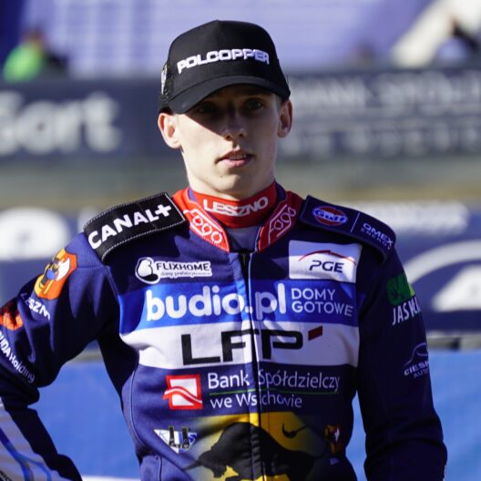 Portrait of a Motorcycle Racer in a Navy Blue Racing Suit with Sponsor Patches and a Black Cap at a Race Track Finish Area 9 Września 2025  ml 3429