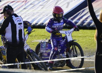 Motocross Race Scene with a Rider in Purple Gear and Red Helmet on a Blue Bike Paused Near the Track While Two People Stand Nearby 23 Lipca 2023 