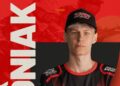 Portrait of a Young Athlete Wearing a Black Cap and Red and black Jersey Facing the Camera Against a Bold Red Backdrop with Large White Text on the Left 15 Czerwca 2020