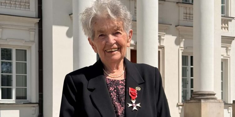 Smiling Elderly Woman in a Black Blazer with a Red Ribbon Medal Standing Outside a White Columned Building 28 Maja 2026