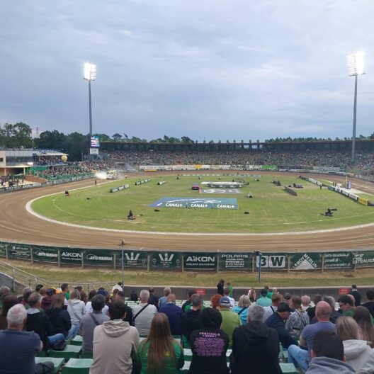 Crowded Outdoor Stadium with a Dirt Race Track Curved Turns and Tall Floodlights Overhead 9 Września 2025