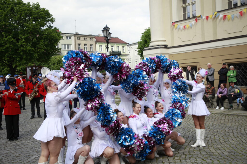 Cheerleaders in White Dresses Performing with Blue and Pink Pom poms in a Street Parade Band in Red Uniforms and Spectators in the Background 9 Września 2025