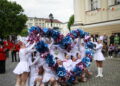 Cheerleaders in White Dresses Performing with Blue and Pink Pom poms in a Street Parade Band in Red Uniforms and Spectators in the Background 15 Czerwca 2020
