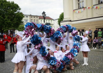 Cheerleaders in White Dresses Performing with Blue and Pink Pom poms in a Street Parade Band in Red Uniforms and Spectators in the Background 5 Maja 2020 