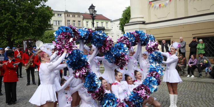 Cheerleaders in White Dresses Performing with Blue and Pink Pom poms in a Street Parade Band in Red Uniforms and Spectators in the Background 10 Maja 2026 