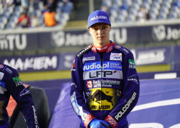 Three Motorcycle Racers in Purple Racing Suits Standing on a Podium with Sponsor Logos Citytrack Backdrop and Blurred Spectators Behind Them Center Rider Looking Ahead Wearing a Blue Cap 26 Listopada 2024