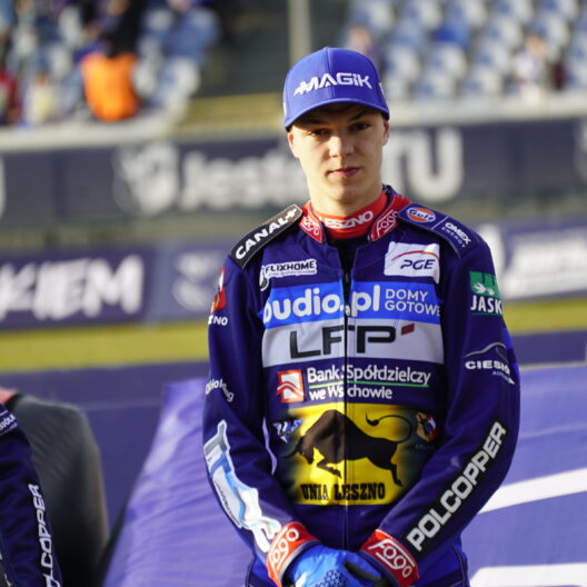 Three Motorcycle Racers in Purple Racing Suits Standing on a Podium with Sponsor Logos Citytrack Backdrop and Blurred Spectators Behind Them Center Rider Looking Ahead Wearing a Blue Cap 9 Września 2025