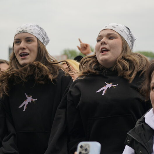 Group of Young People Cheering at an Outdoor Event Two Central Girls Wear White Bandanas and Black Hoodies 9 Września 2025