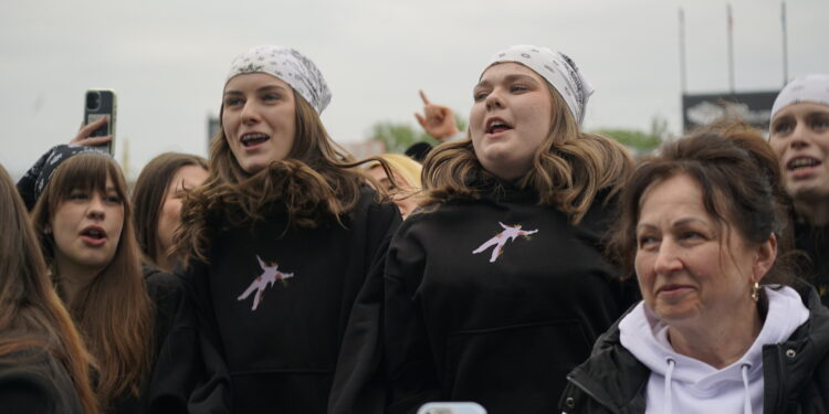 Group of Young People Cheering at an Outdoor Event Two Central Girls Wear White Bandanas and Black Hoodies 10 Maja 2026 