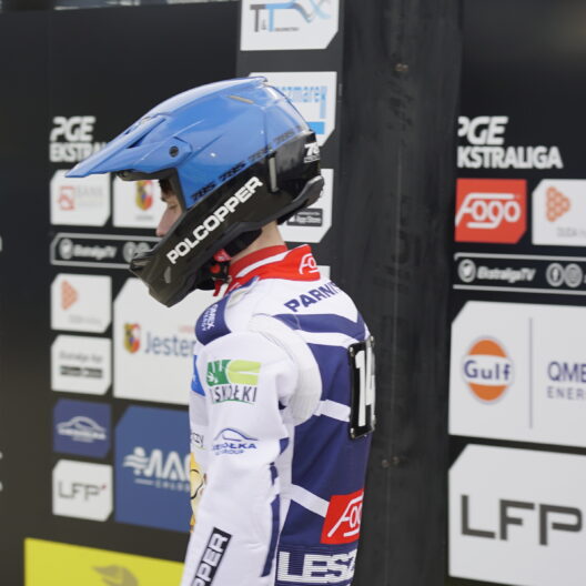Motorsport Rider in a Blue Helmet and White Racing Suit Stands at a Sponsor filled Pit Wall 9 Września 2025  ml 5067