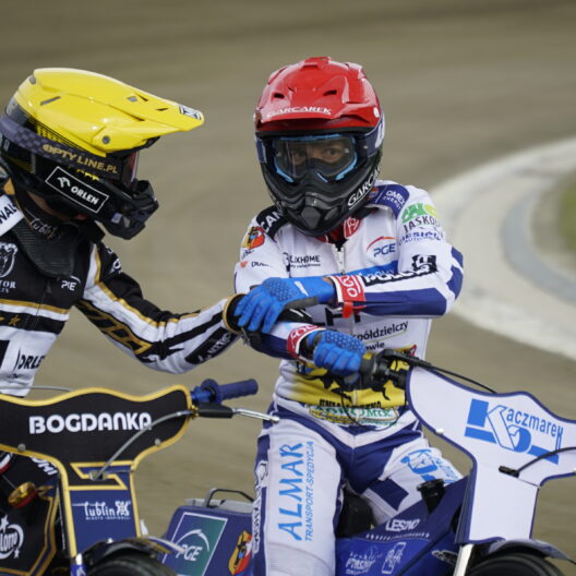 Two Speedway Riders in Colorful Racing Suits on a Dirt Track Shaking Hands Mid race or After a Heat Their Bikes Visible in the Foreground 9 Września 2025  ml 5210