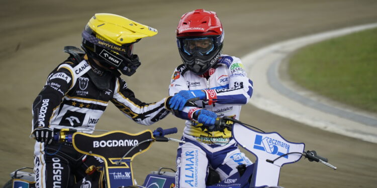 Two Speedway Riders in Colorful Racing Suits on a Dirt Track Shaking Hands Mid race or After a Heat Their Bikes Visible in the Foreground 17 Maja 2026  ml 5210