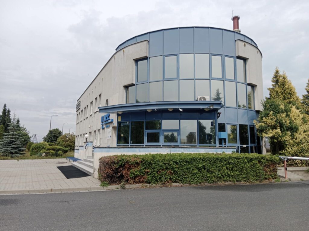 Curved Blue glass Office Building with Blue Framing Set on a Paved Plaza and Hedges Around It 9 Września 2025