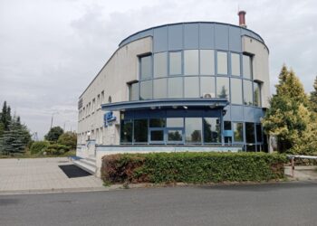 Curved Blue glass Office Building with Blue Framing Set on a Paved Plaza and Hedges Around It 10 Lipca 2019