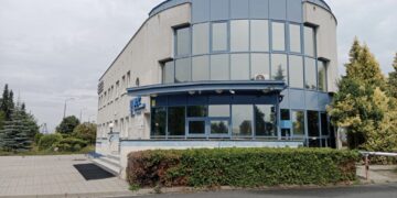 Curved Blue glass Office Building with Blue Framing Set on a Paved Plaza and Hedges Around It 12 Czerwca 2020