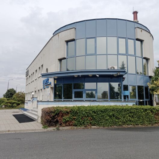 Curved Blue glass Office Building with Blue Framing Set on a Paved Plaza and Hedges Around It 9 Września 2025