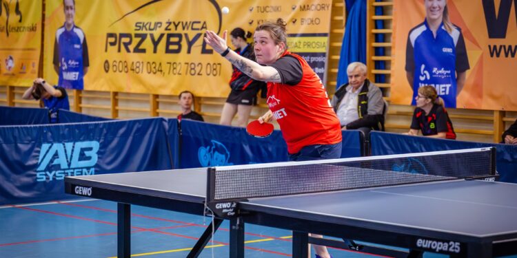 Female Table Tennis Player in a Red Shirt Reaching to Return the Ball During a Match in an Indoor Gym with Banners in the Background 4 Maja 2026 