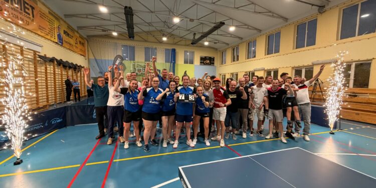 Group of Athletes Posing for a Celebration Photo in a Gymnasium Many Raising Their Arms and Cheering with Banners on the Wall Behind Them and Sparklers at the Sides 25 Maja 2026