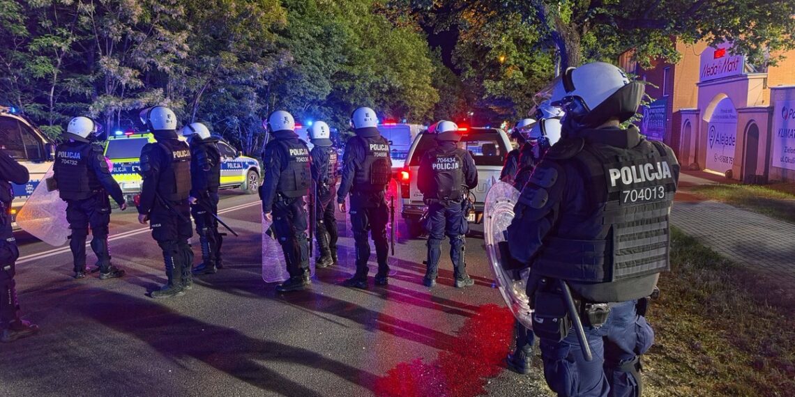 Line of Riot Police in Body Armor and Helmets with Shields Standing on a City Street at Night Blue and Red Flashing Patrol Lights in the Background 16 Czerwca 2020