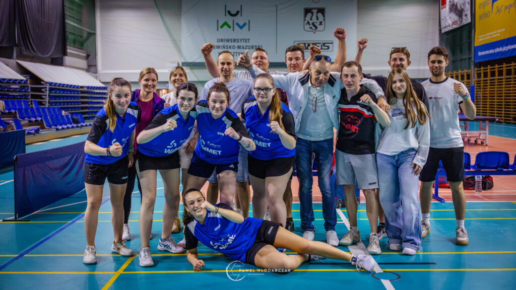 a Group of Athletes and Coaches Posing for a Team Photo in an Indoor Sports Hall Many Raising Fists and Smiling 9 Września 2025