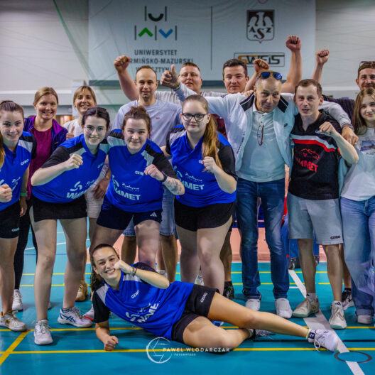 a Group of Athletes and Coaches Posing for a Team Photo in an Indoor Sports Hall Many Raising Fists and Smiling 9 Września 2025