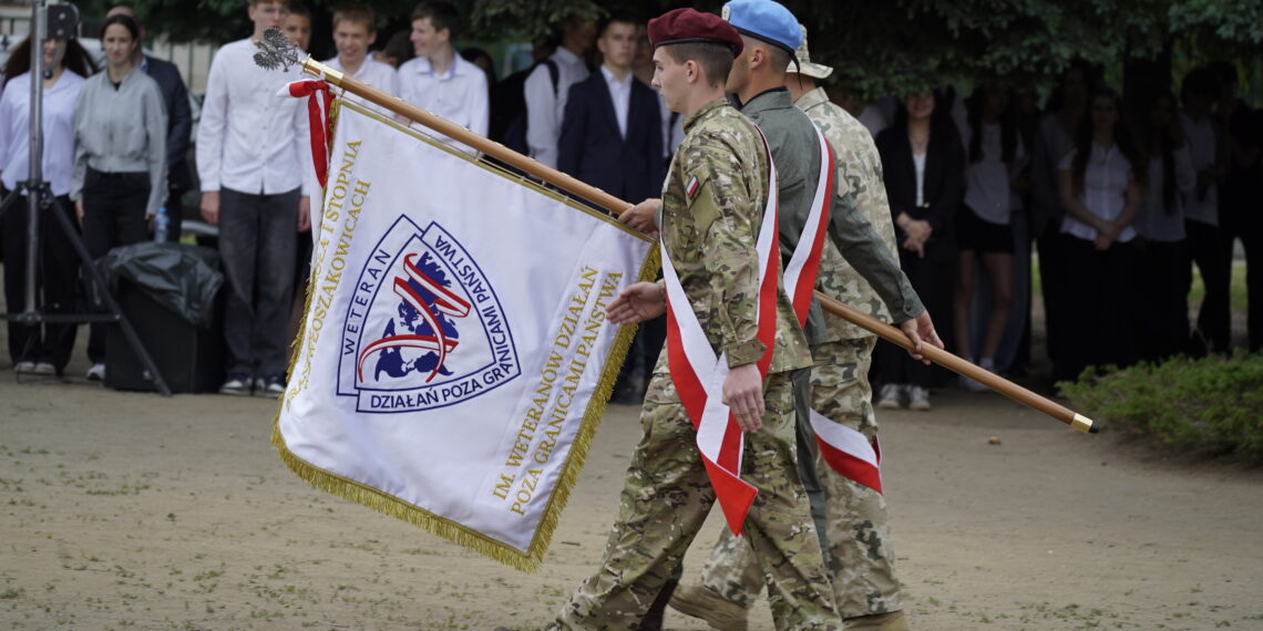 Soldiers in Camouflage March While Carrying a Large Ceremonial Flag with Red and white Ribbons at an Outdoor Event a Crowd Stands in the Background 16 Czerwca 2020
