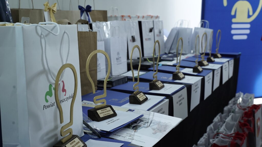 Row of Award Trophies and Gift Bags Lined Up on a Blue Table at an Awards Ceremony with a Blue Backdrop in the Background 9 Września 2025  ml 5750