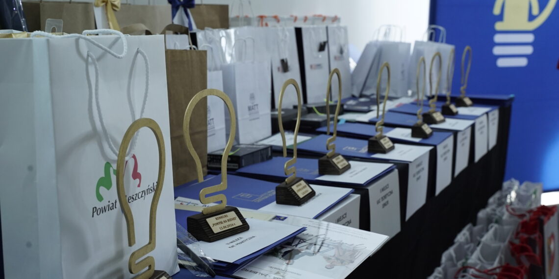 Row of Award Trophies and Gift Bags Lined Up on a Blue Table at an Awards Ceremony with a Blue Backdrop in the Background 15 Czerwca 2020  ml 5750