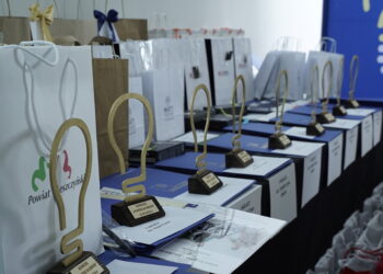 Row of Award Trophies and Gift Bags Lined Up on a Blue Table at an Awards Ceremony with a Blue Backdrop in the Background 12 Września 2024  ml 5750