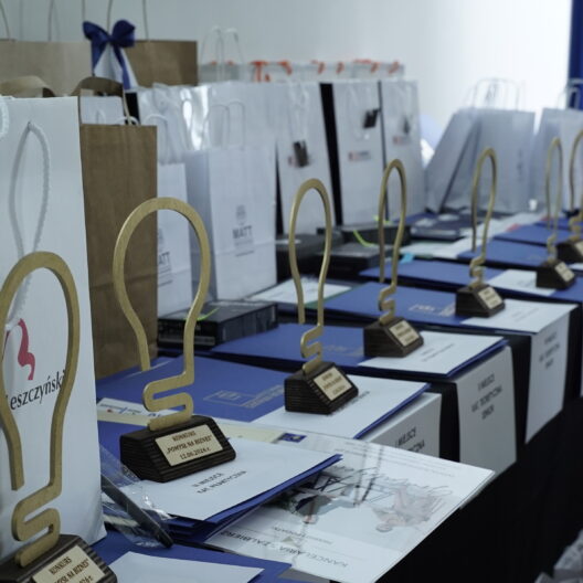 Row of Award Trophies and Gift Bags Lined Up on a Blue Table at an Awards Ceremony with a Blue Backdrop in the Background 9 Września 2025  ml 5750