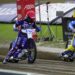 Three Speedway Riders in Blue and Yellow Suits Race on a Muddy Track Kicking Up Dirt As They Round a Bend with Banners in the Background 15 Czerwca 2020