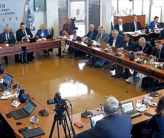 City Council Meeting with Officials Seated Around a U shaped Table Laptops and Microphones in Use a Camera Recording the Session in Progress 9 Września 2025